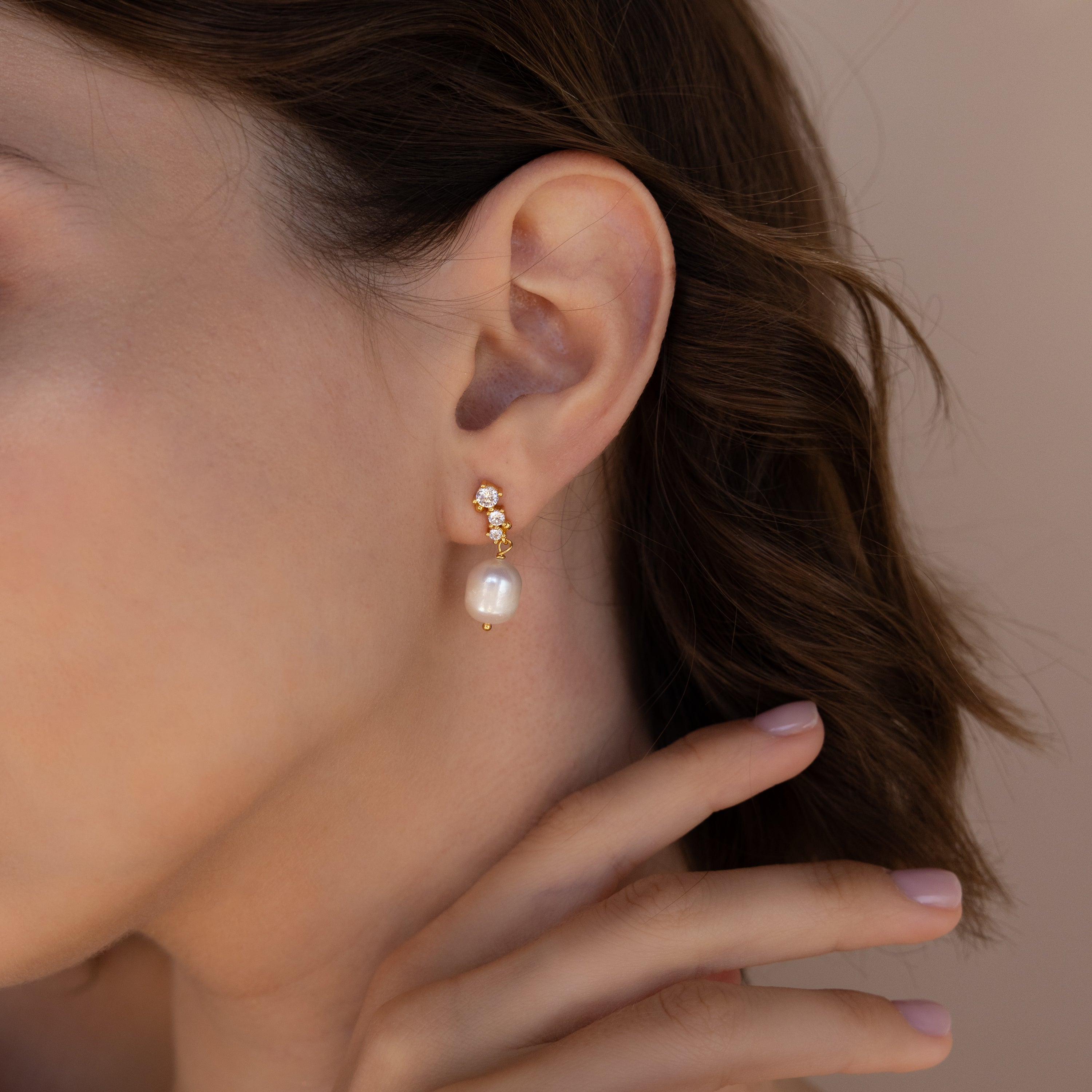 A close-up of a woman wearing one gold Millie Drop Earring, showcasing the delicate sparkle of the crystals and the elegant pearl drop.
