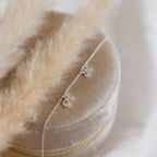 The Mellow Dainty Initial Necklace, featuring two elegant cursive S charms, sits atop a beige velvet jewelry box with soft pampas grass beside it.