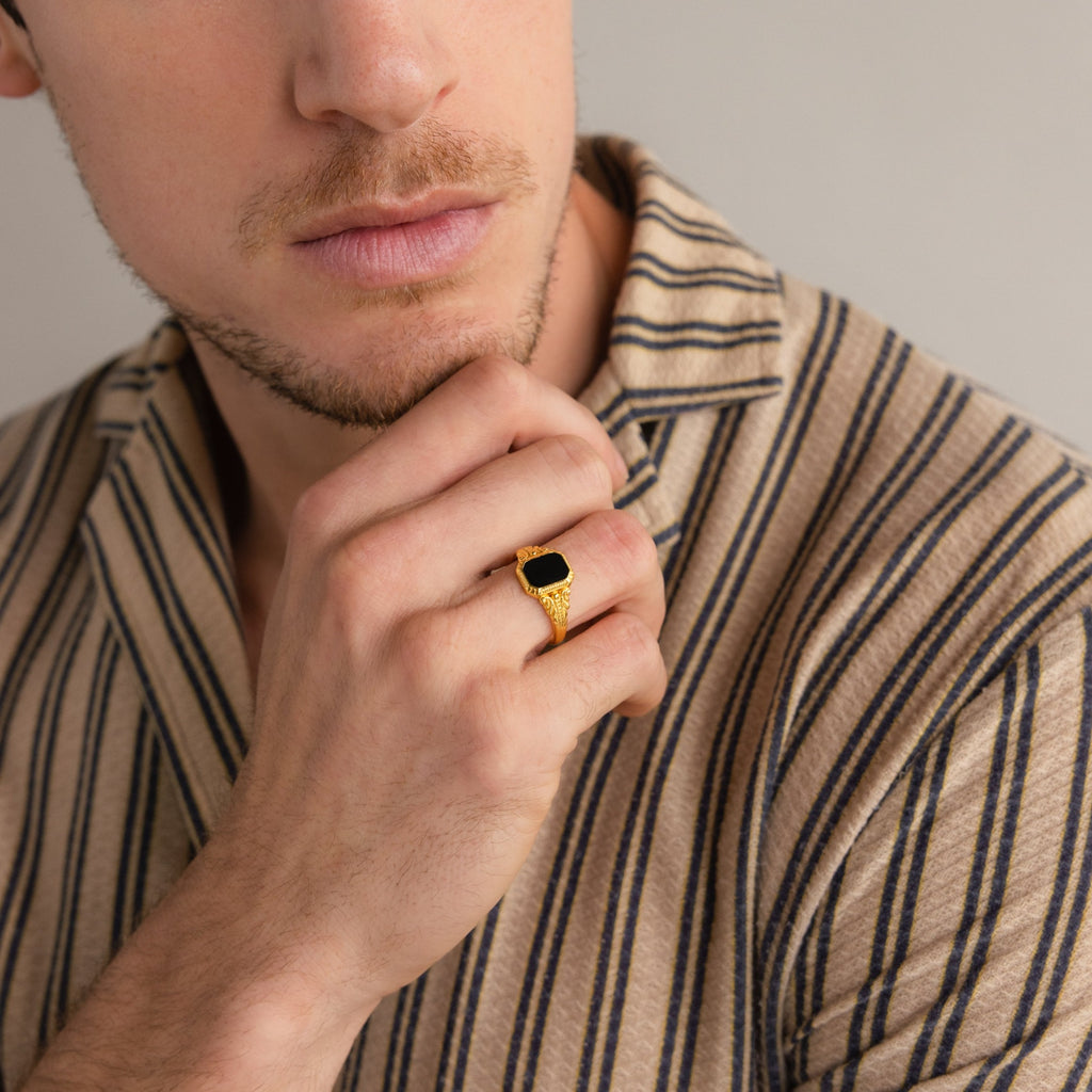 A man in a striped shirt touches his chin, highlighting the Vintage Black Signet Ring on his finger.
