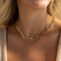 Close-up of a woman wearing the Herringbone Duo Chain Necklace in 18K Gold layered with a box chain, styled with a textured beige top and blonde hair.