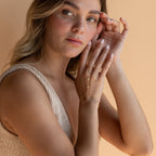 A woman with light brown hair wearing a knitted top and the Diamond Bezel Hand Chain poses against a beige background.