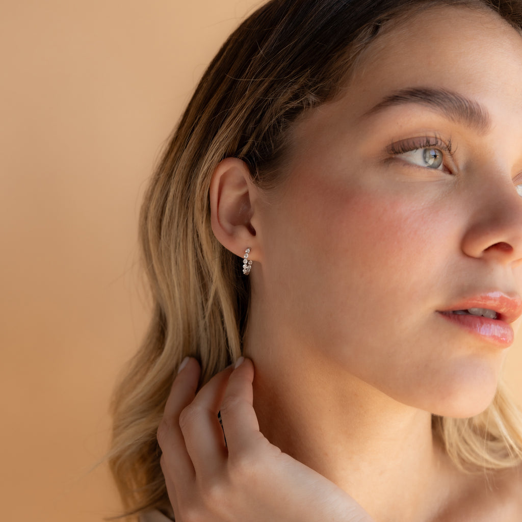 Woman with light hair touches her Inside Out Diamond Huggies in Sterling Silver, gazing to the side against a beige background.