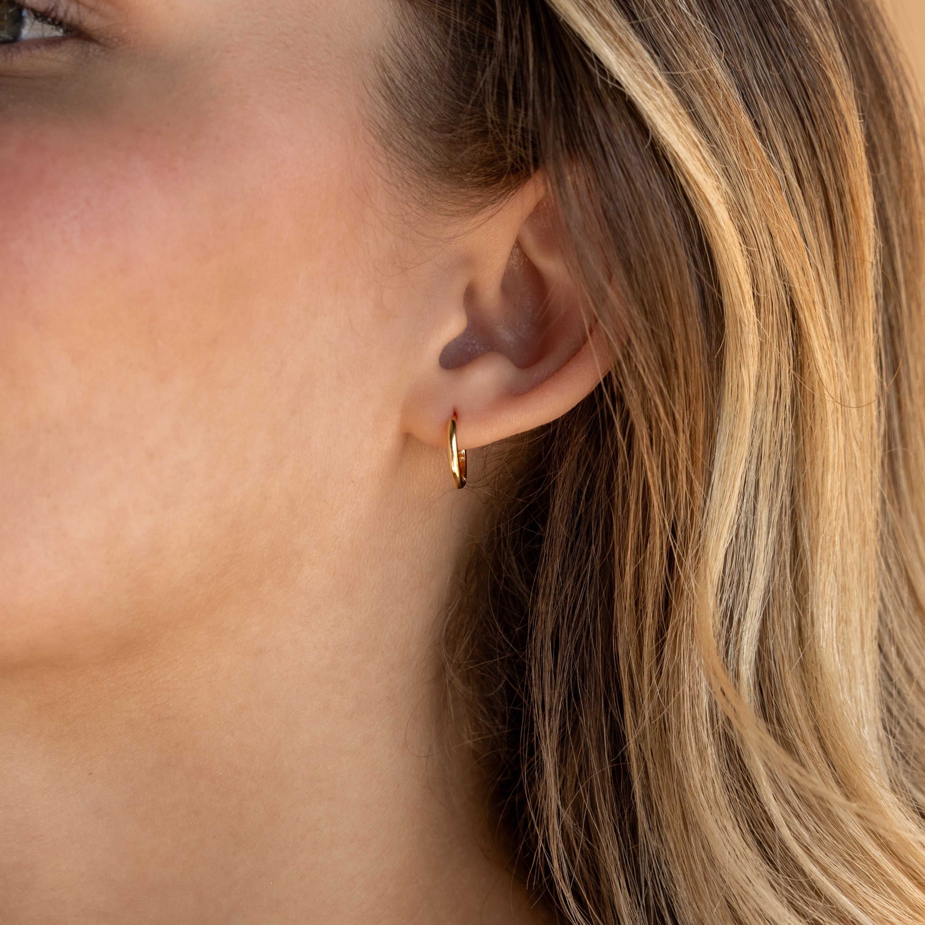 Close-up of a woman's ear adorned with Small Bold Hoops—minimalist earrings that look chic with her blonde hair, ideal for daily wear.