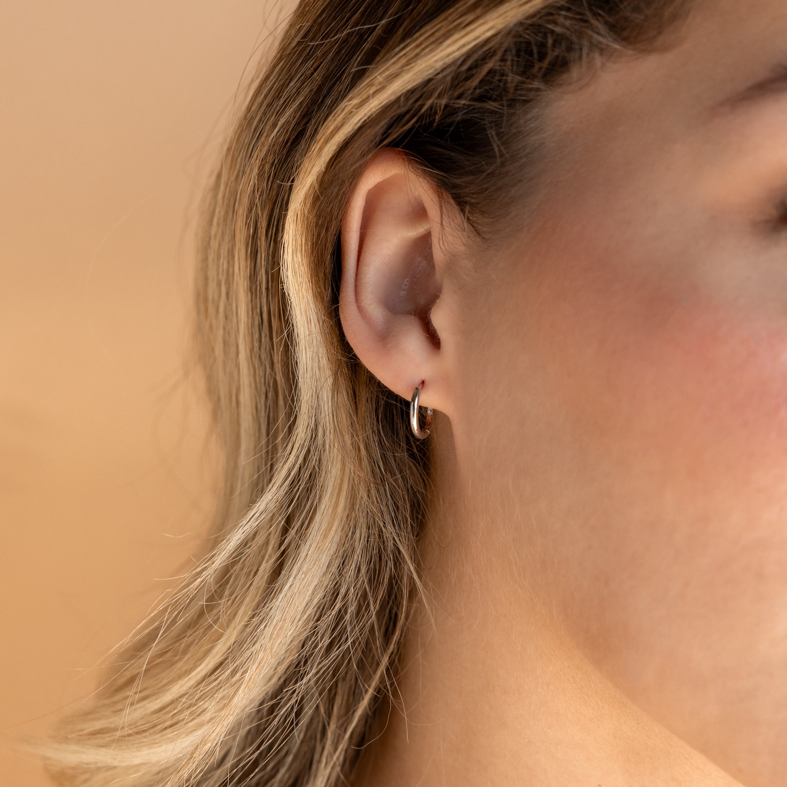 Close-up of a woman's ear wearing the Small Bold Hoops in Sterling Silver—minimalist hoops perfect for everyday wear, with blonde hair partially visible.