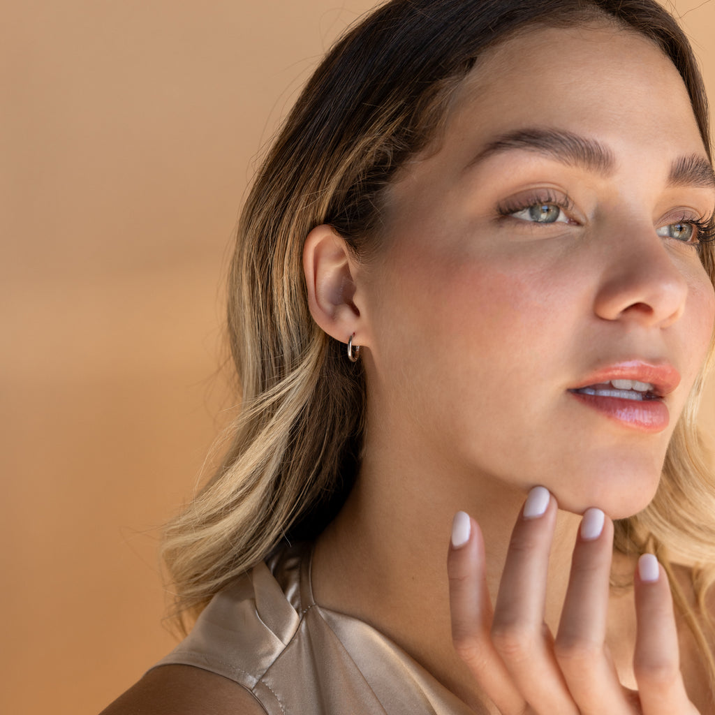 A woman with her hand on her chin showcases the Small Bold Hoops in Sterling Silver, minimalist earrings that add subtle elegance to her everyday look.