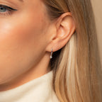 Close-up of a woman's ear wearing Molly Pearl Huggies, sleek hoop earrings featuring a sparkling diamond charm, adding subtle elegance to her look.