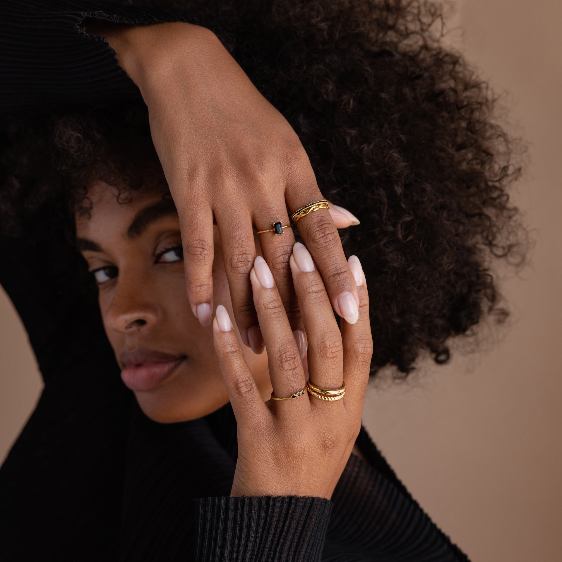 Woman with curly hair displays hands adorned with the Black Emerald Ring in Silver and light pink nails against a beige background.