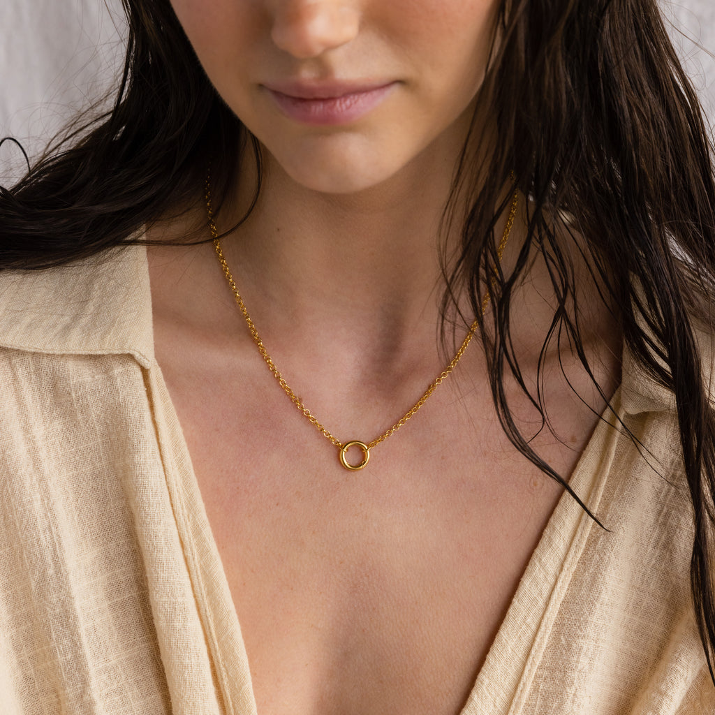 Woman wearing a beige top and the Rolo Circle Charm Necklace in 18K Gold with a small circular pendant, shown from the shoulders up—a perfect minimalist necklace look.