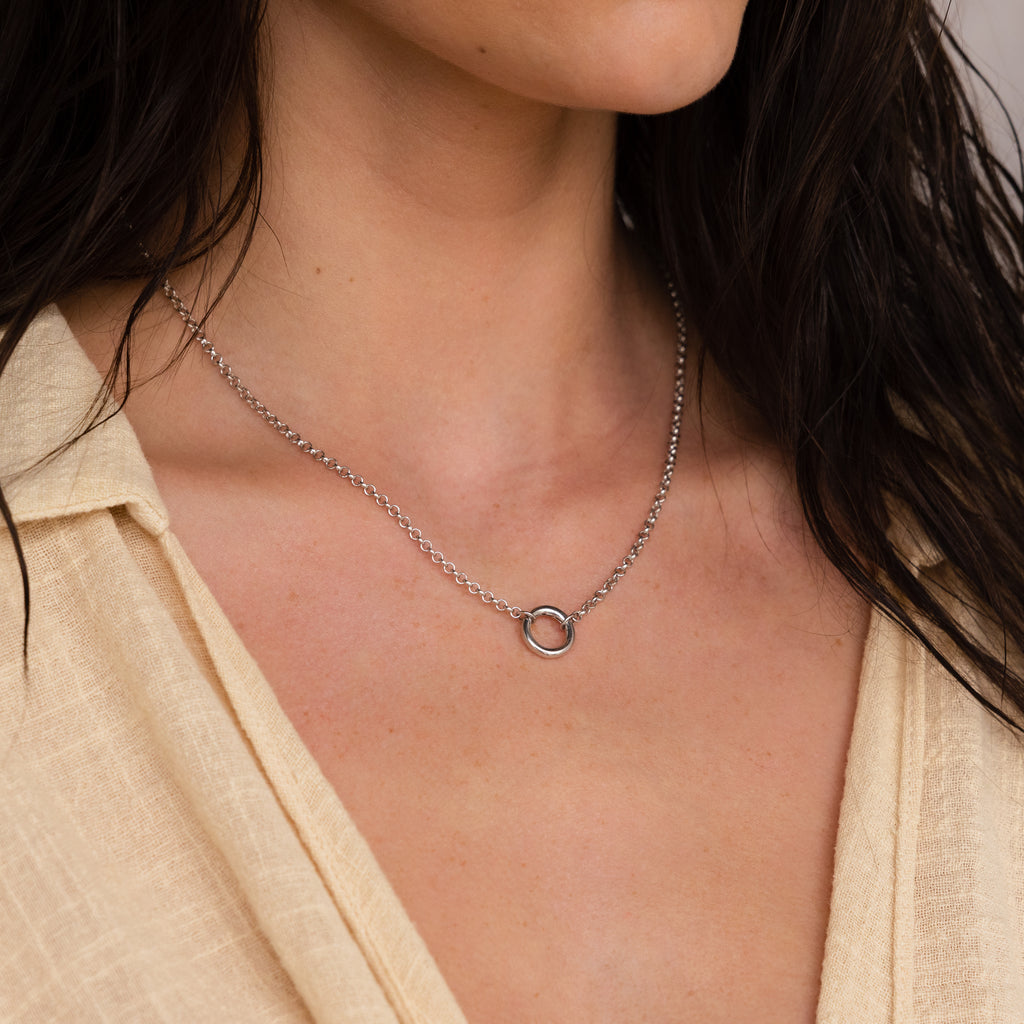 A woman in a cream-colored top wears the Rolo Circle Charm Necklace in Sterling Silver, featuring a customizable circular pendant on a silver Rolo Link Chain.