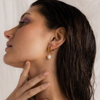 A woman wearing the Dangling Pearl Drop Earring in gold, styled with two additional gold hoop earrings on the same ear.