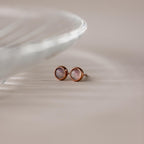 Moonstone Bezel Studs: round, rose gold studs with iridescent moonstones, shown on a neutral surface by a glass dish—ideal for fans of subtle jewelry.