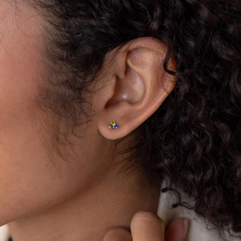 Close-up of a person's ear with curly hair, wearing a Toi et Moi Baguette Birthstone Stud earring featuring colorful details.