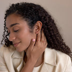 Woman with curly hair wearing a cream blazer and a gold ring with red stones showcases sparkling Toi et Moi Baguette Birthstone Studs.