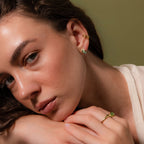 Woman wearing small gold stud earrings with smooth green jade drops, a gold ear cuff, and a matching jade ring.