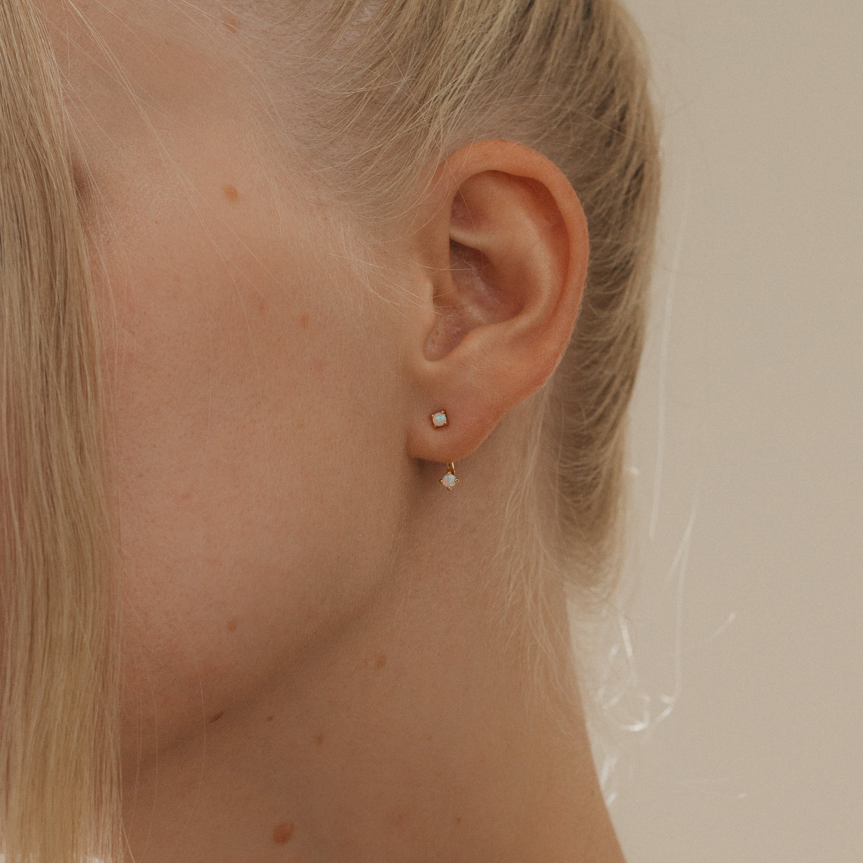 Close‑up of a model’s ear wearing a opal gold birthstone ear jacket with its matching back‑facing CZ gemstone creating a layered look.