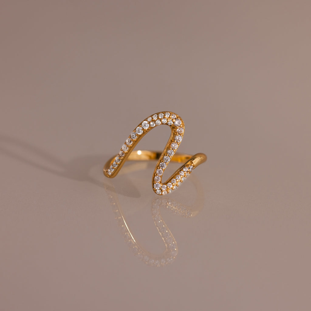 Pave Wave Ring featuring a wavy, abstract gold design encrusted with small diamonds, ideal for stacking and beautifully set against a neutral background.