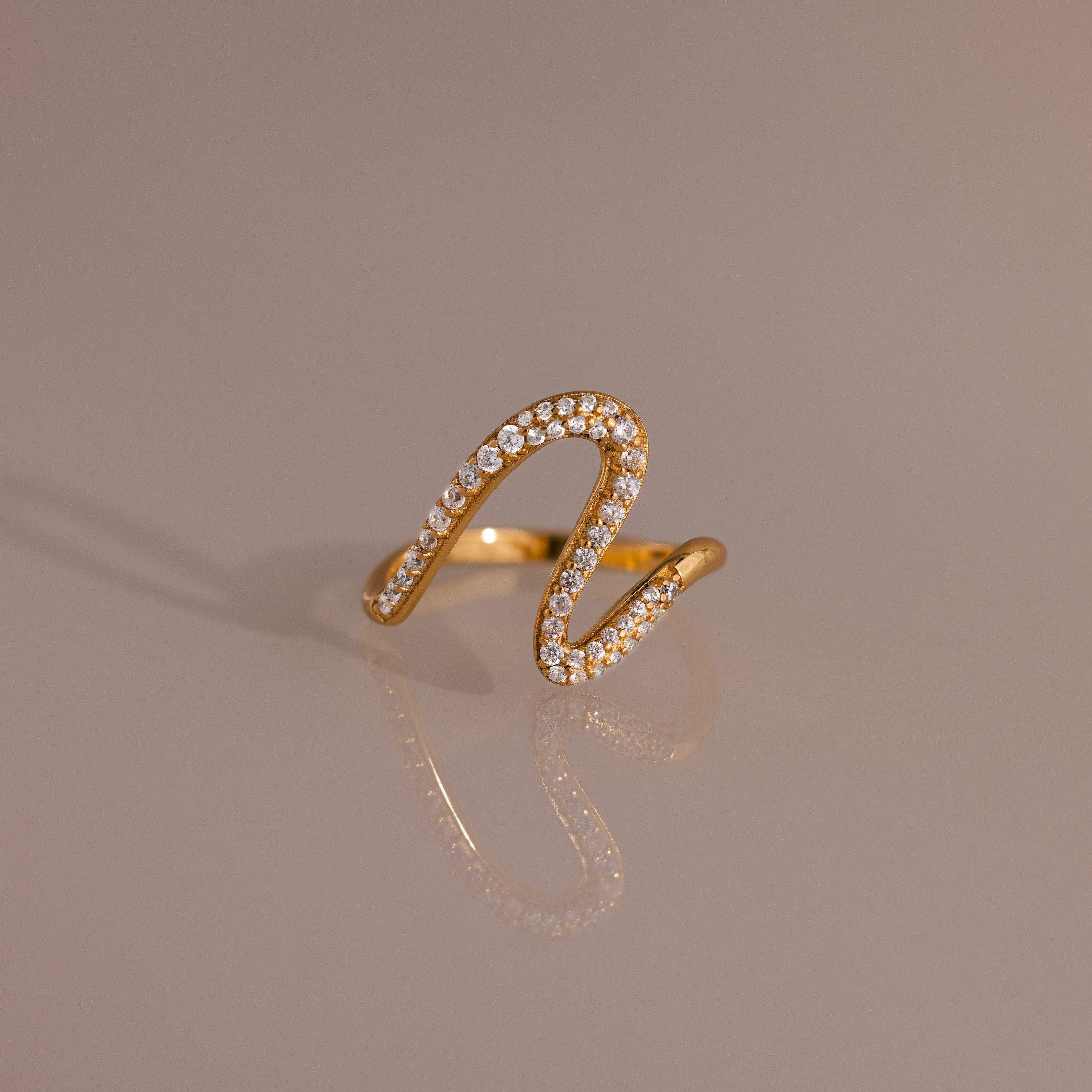 Pave Wave Ring featuring a wavy, abstract gold design encrusted with small diamonds, ideal for stacking and beautifully set against a neutral background.