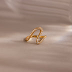 The Pave Wave Ring, featuring a gold wavy design encrusted with small diamonds, is shown on a soft beige background—ideal for stacking and adding subtle elegance to any look.