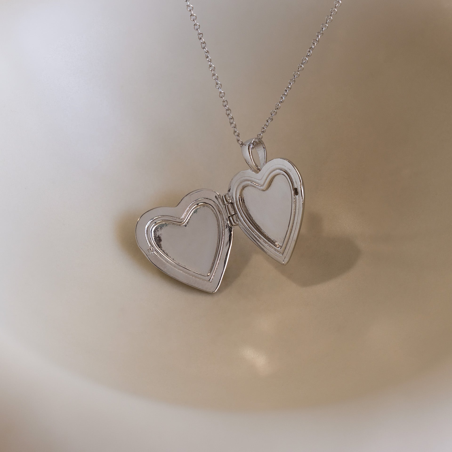 Up close of silver heart-shaped locket pendant necklace opened up and displayed on a ceramic surface.