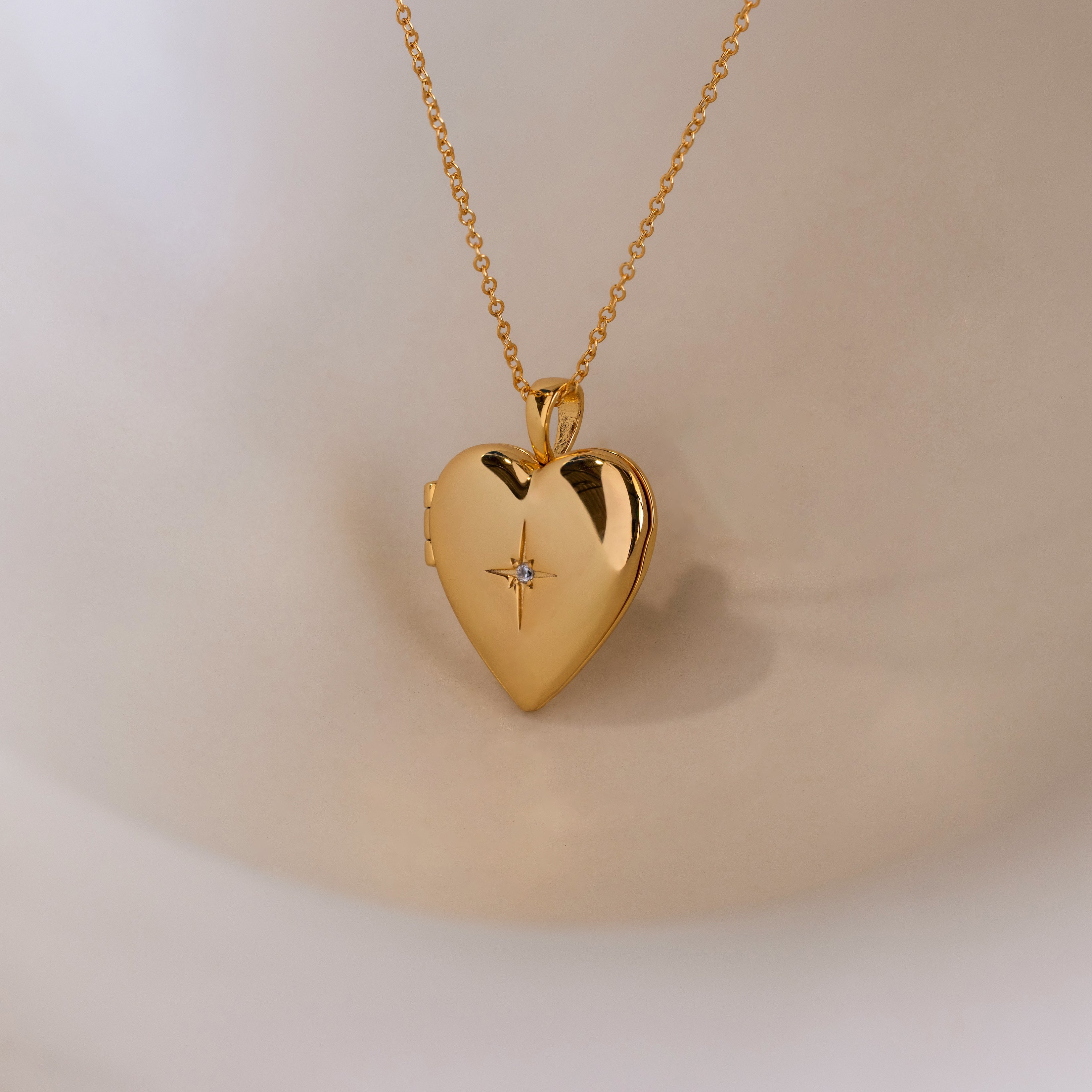 A gold heart-shaped locket with a north star CZ diamond in the center on a delicate cable chain.