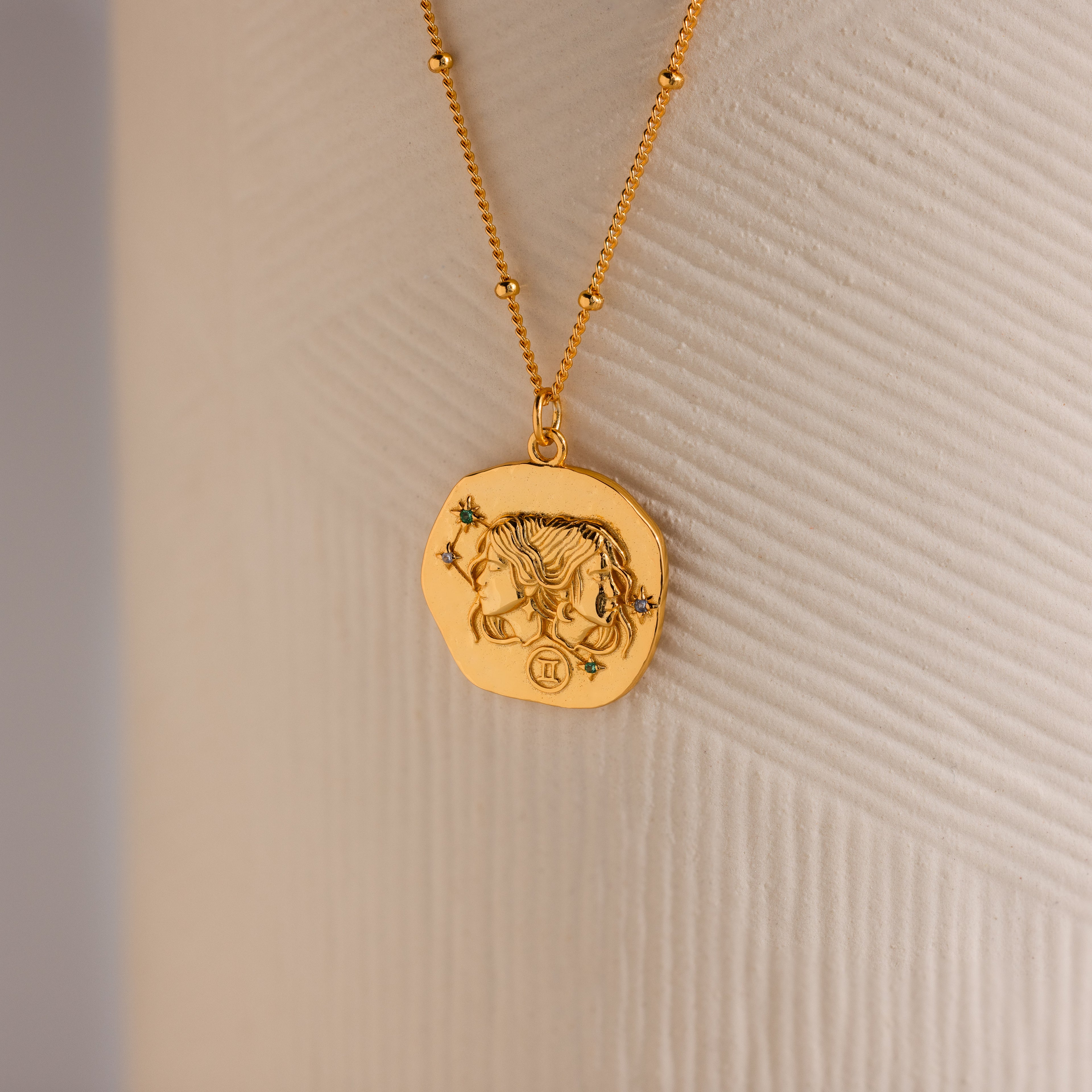 Close up of a Gold 3D Gemini Zodiac Coin Pendant Necklace with small CZ gemstones, attached to a dainty satellite chain.