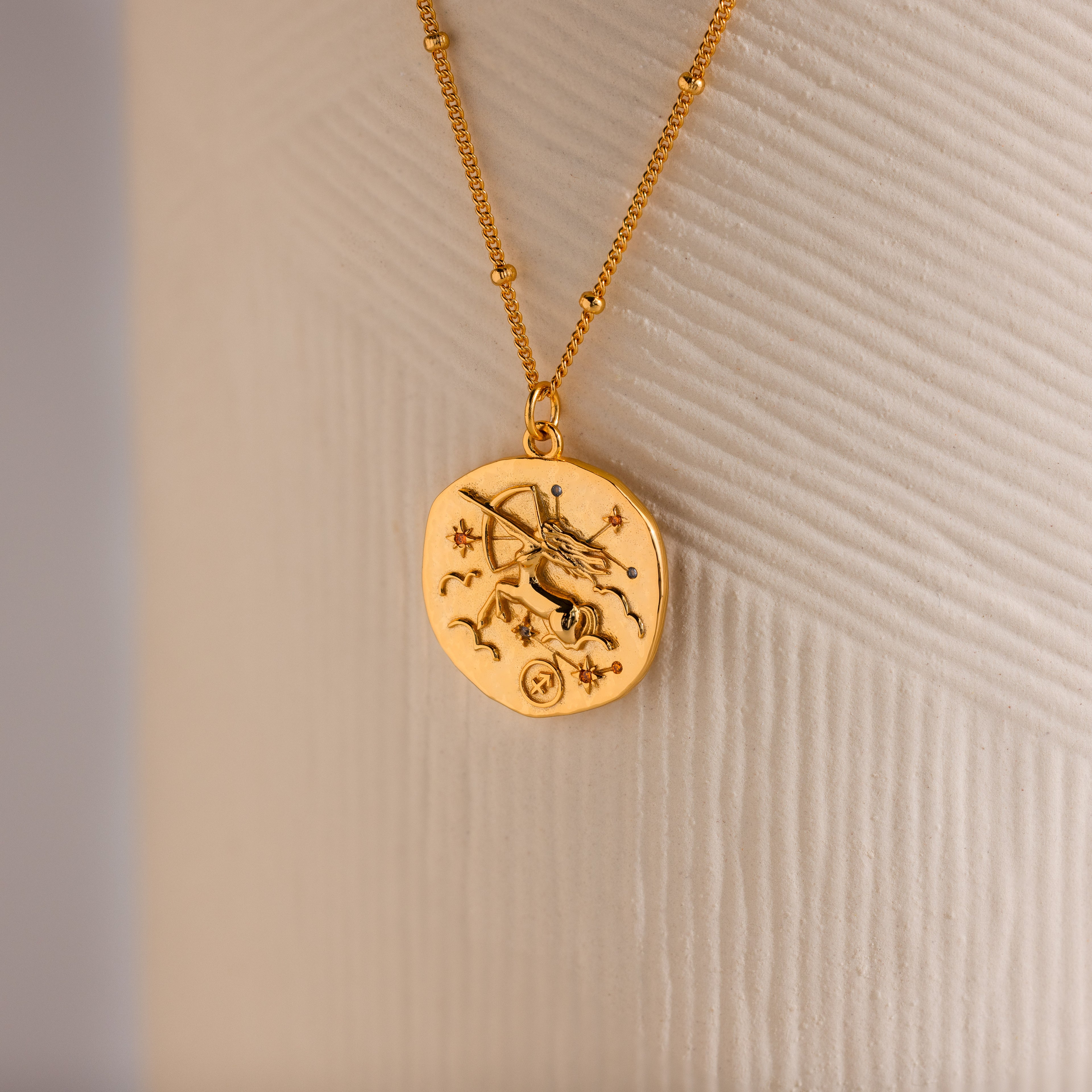 Close up of a Gold 3D Sagittarius Zodiac Coin Pendant Necklace with small CZ gemstones, attached to a dainty satellite chain.