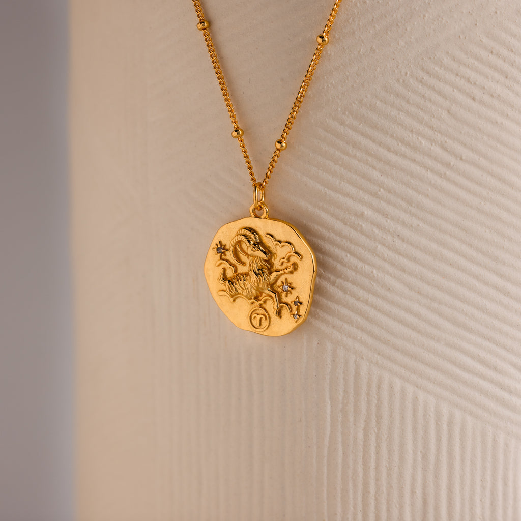 Close up of a Gold 3D Aries Zodiac Coin Pendant Necklace with small CZ gemstones, attached to a dainty satellite chain.