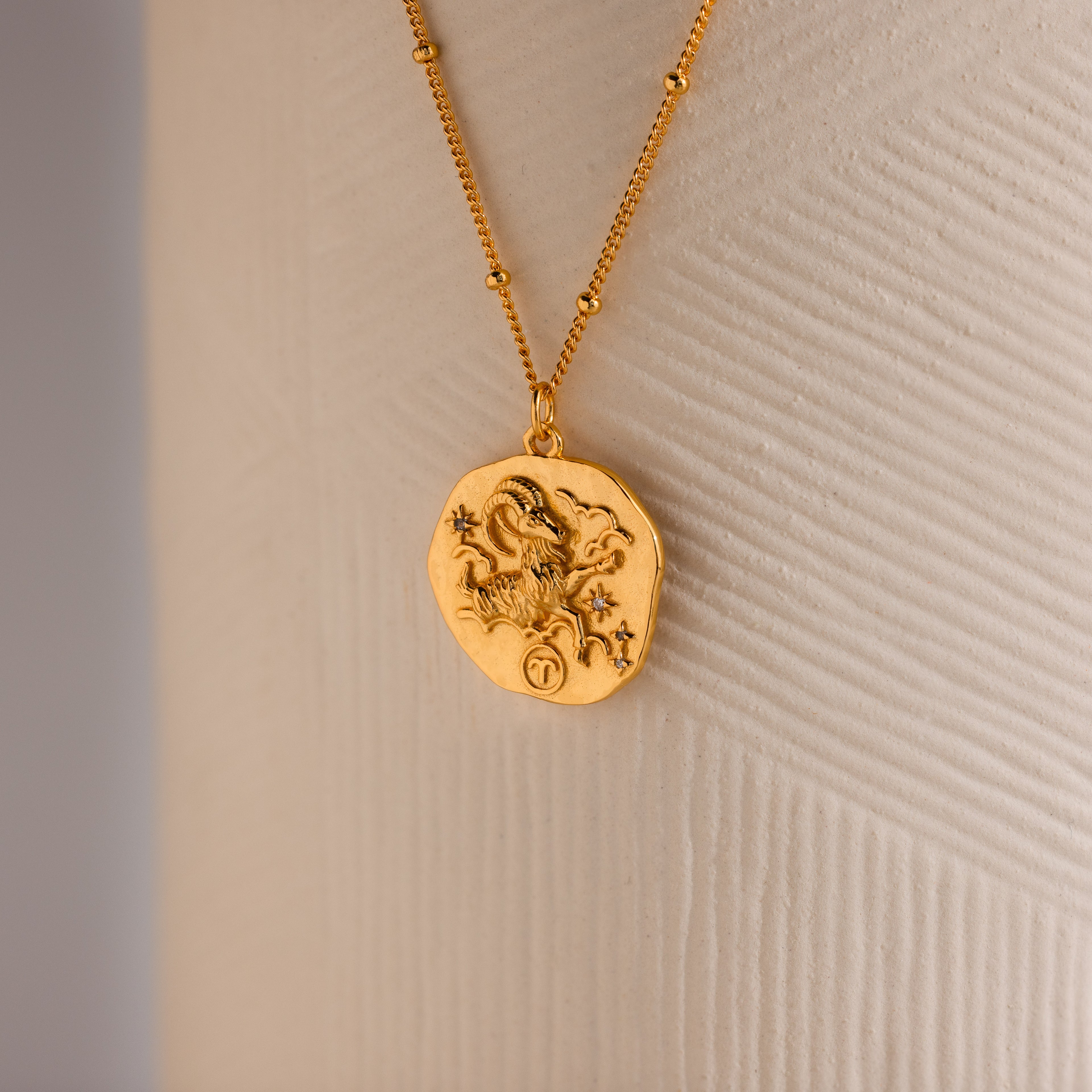 Close up of a Gold 3D Aries Zodiac Coin Pendant Necklace with small CZ gemstones, attached to a dainty satellite chain.
