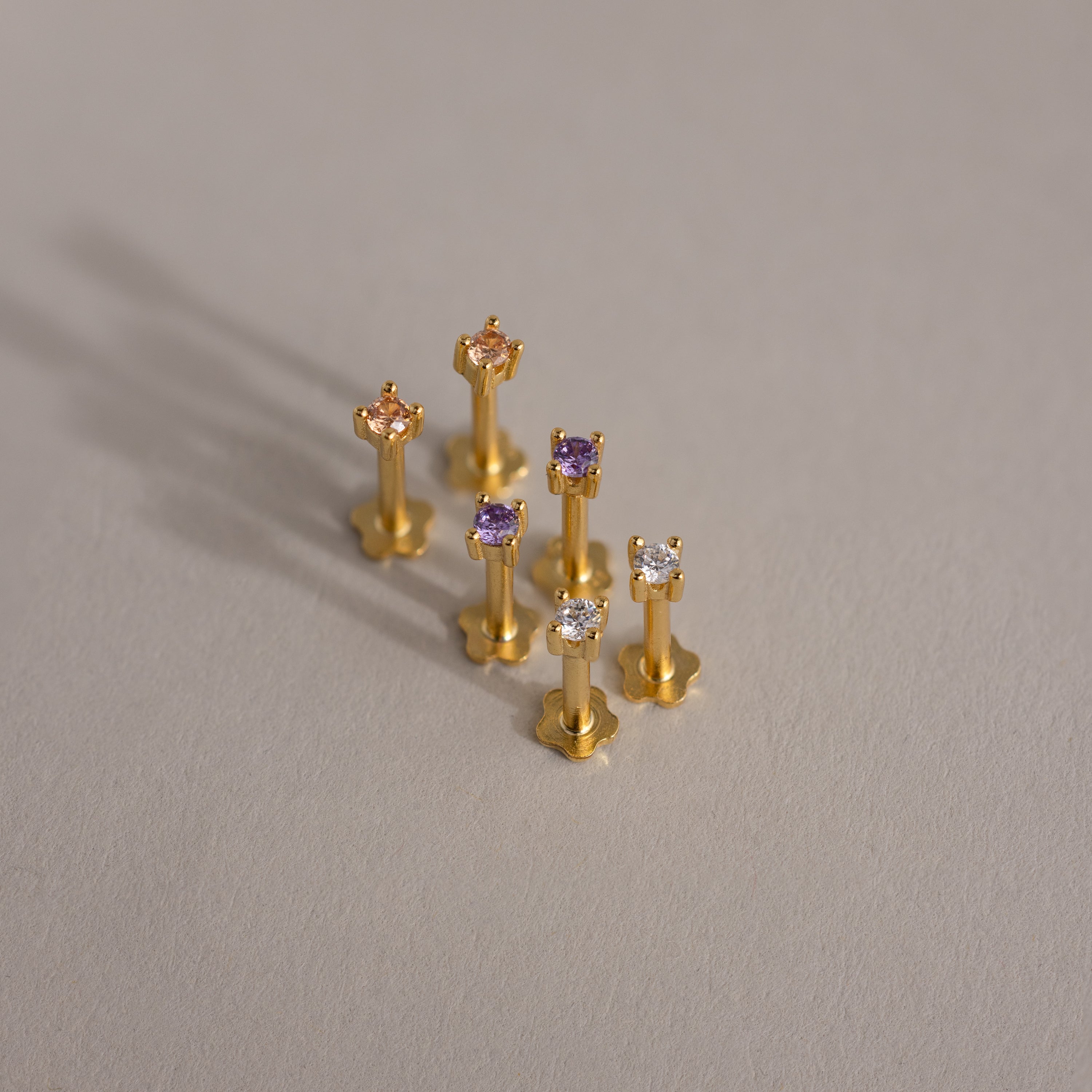 Six Dainty Birthstone Flatback Studs with colorful gemstones are displayed on a light gray surface—a timeless choice, perfect for stacking and multiple piercings.