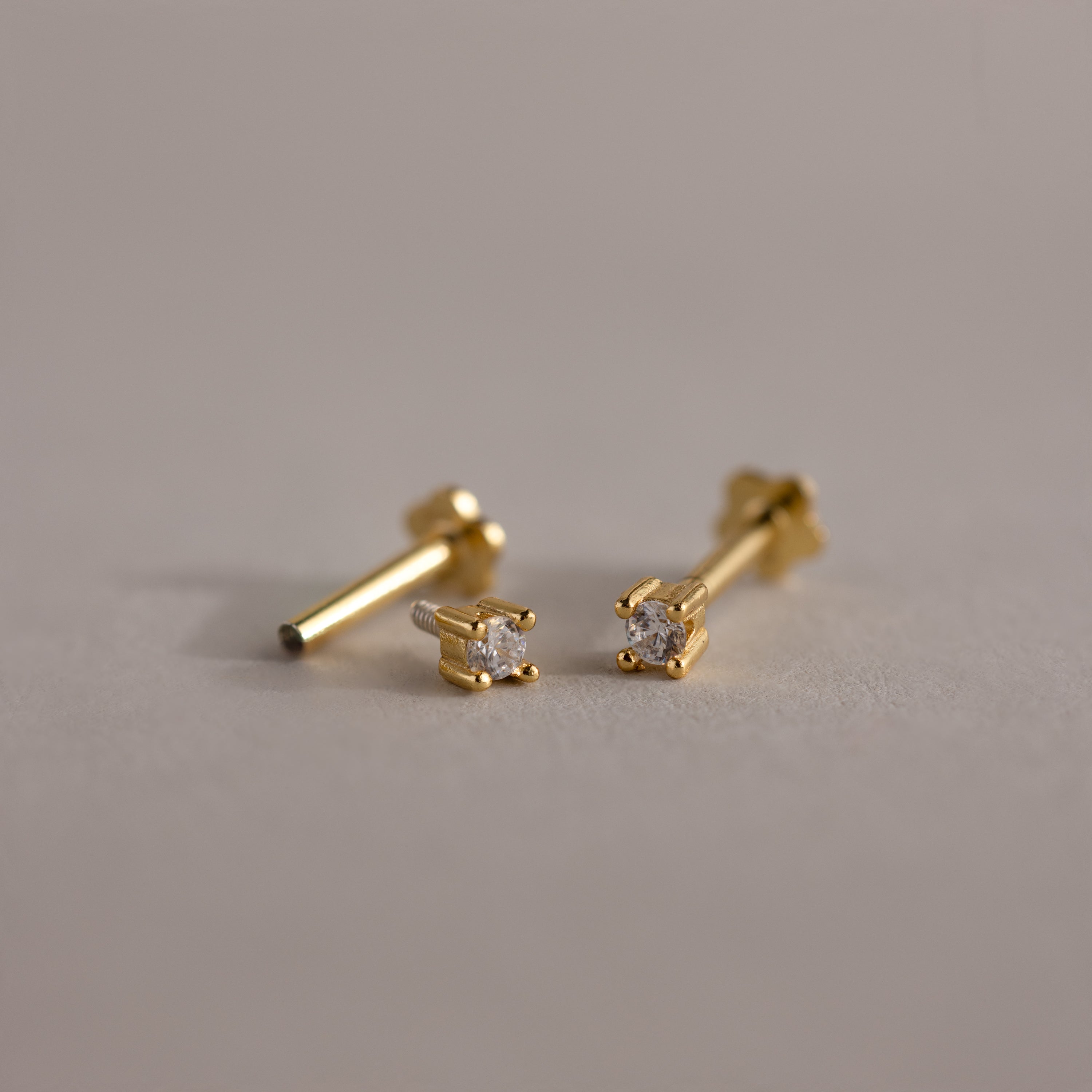 Dainty Diamond Flatback Studs—small gold earrings with clear round gemstones, perfect for multiple piercings—shown on a neutral background.
