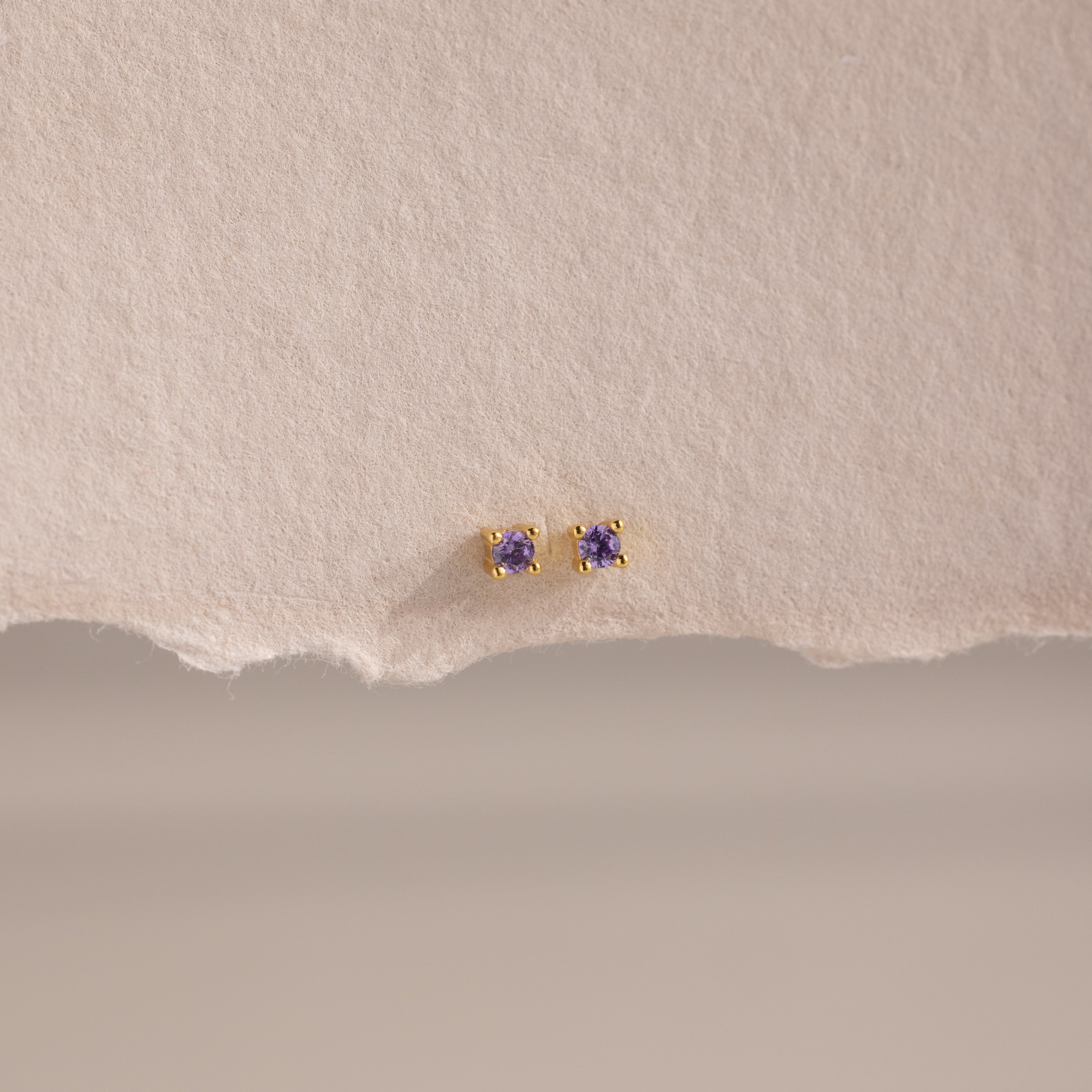Dainty Amethyst Flatback Studs featuring small purple gemstones, perfect for multiple piercings, shown on a textured beige paper background.