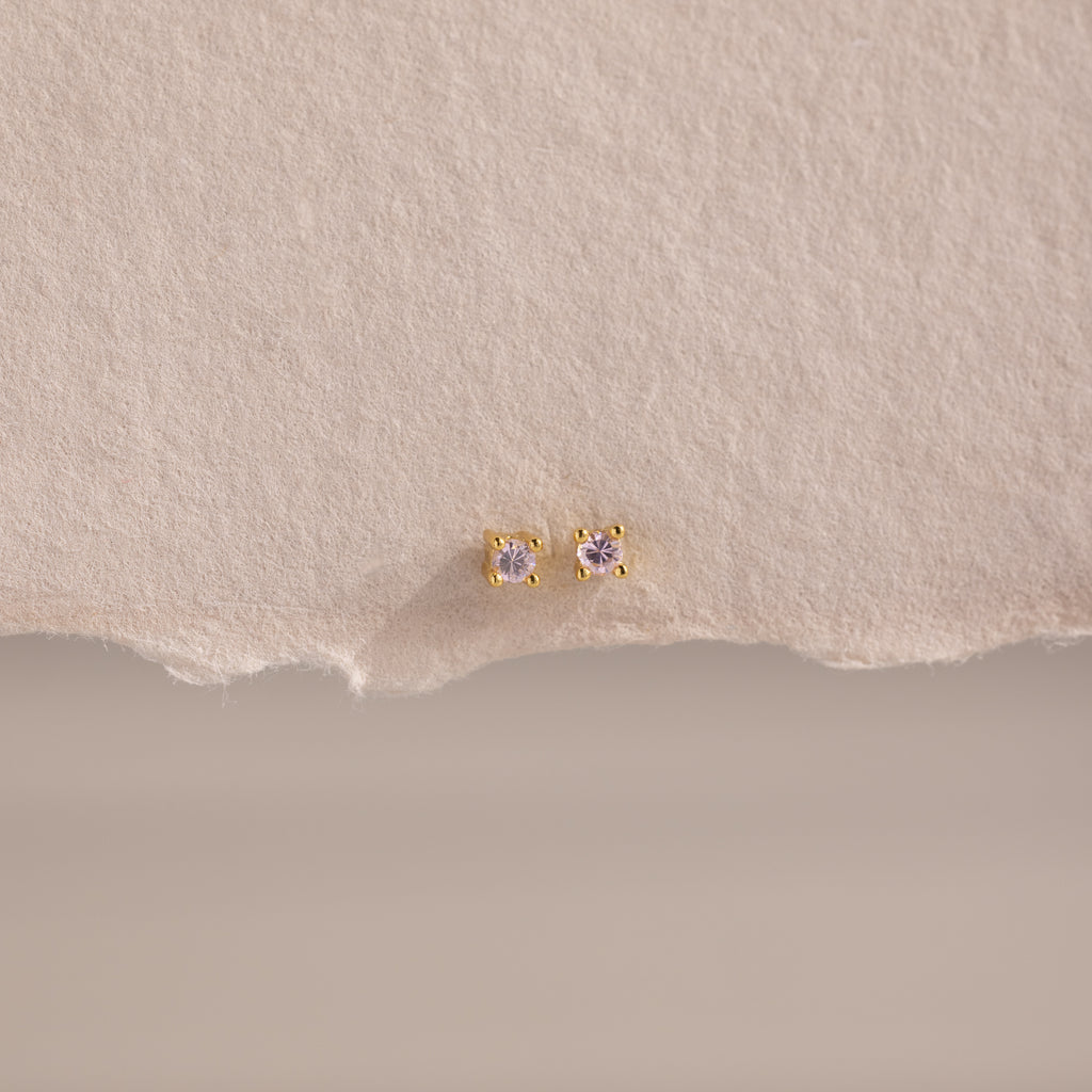 Dainty Pink Tourmaline Flatback Studs with delicate pink stones set in gold, ideal for multiple piercings, shown on a textured beige background.