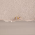 Dainty Pink Tourmaline Flatback Studs with delicate pink stones set in gold, ideal for multiple piercings, shown on a textured beige background.