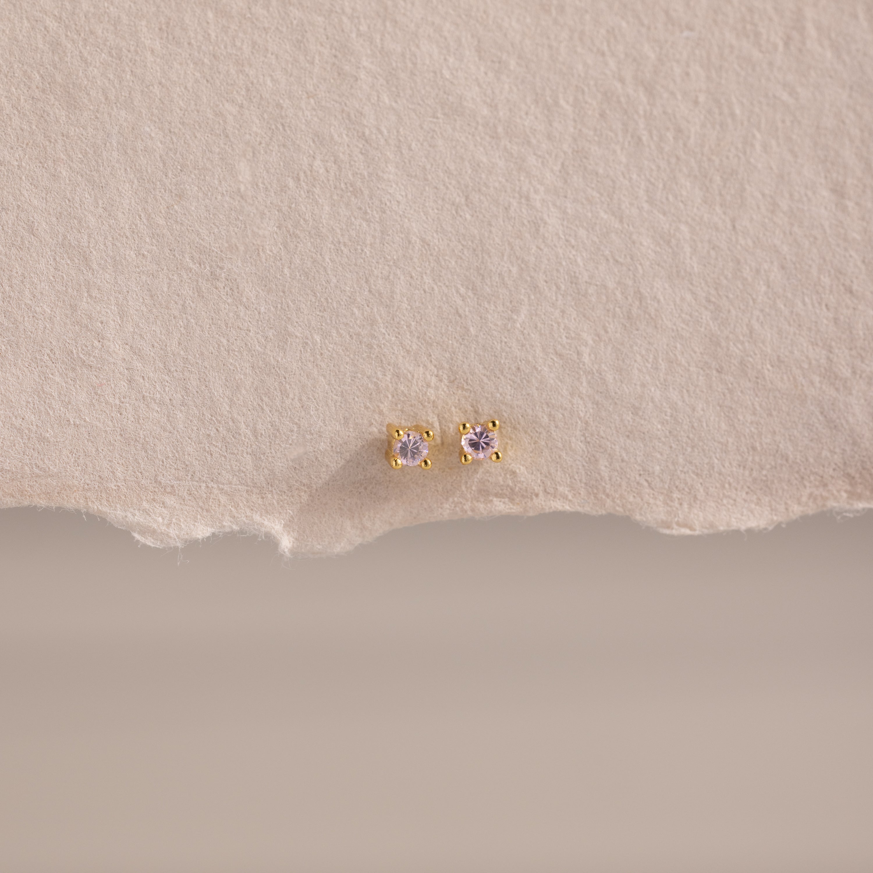 Dainty Pink Tourmaline Flatback Studs with delicate pink stones set in gold, ideal for multiple piercings, shown on a textured beige background.