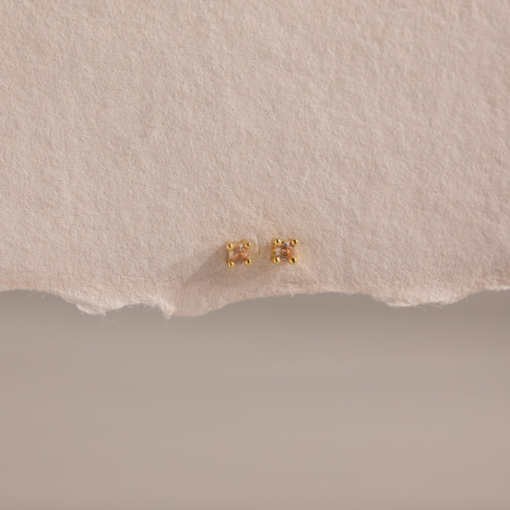 Dainty Topaz Flatback Studs—lightweight gold square earrings, perfect for multiple piercings, shown on a textured beige paper background.