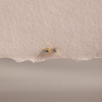 Dainty Aquamarine Flatback Studs with small round aquamarines, perfect for multiple piercings, displayed on textured, torn-edge beige paper.