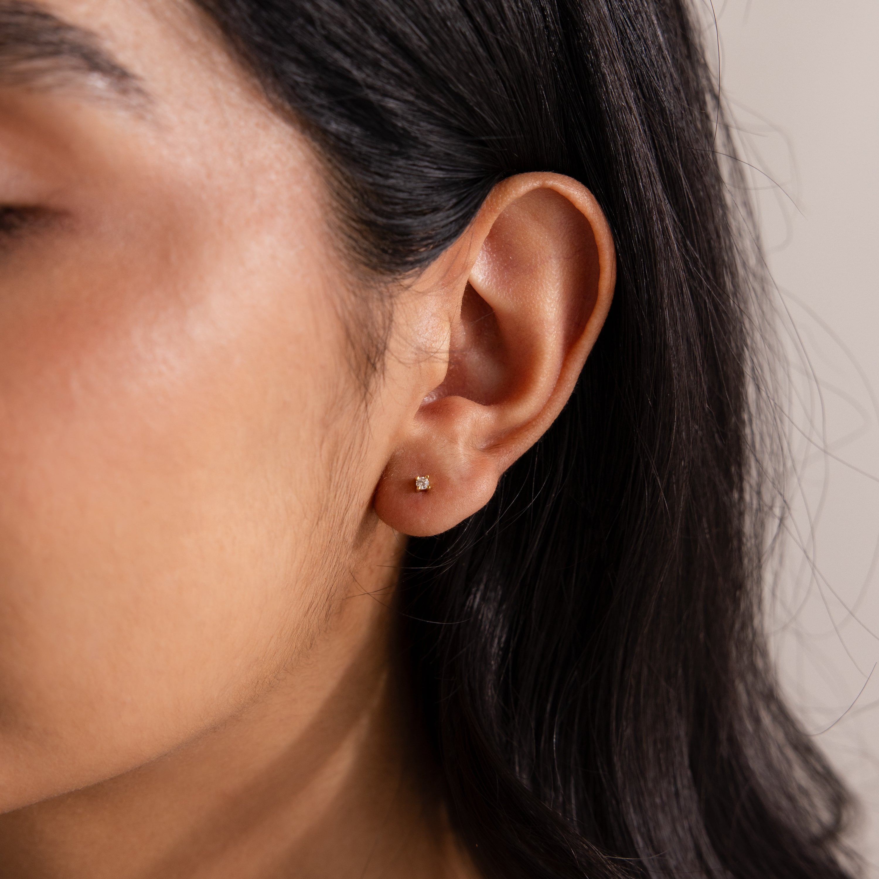 Close-up of a woman's ear with dark hair tucked behind it, highlighting the elegant Dainty Diamond Flatback Studs—small gold earrings perfect for multiple piercings.