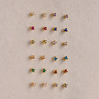 Twenty pairs of Dainty Amethyst Flatback Studs, ideal for multiple piercings, are displayed in a neat grid on a beige surface.