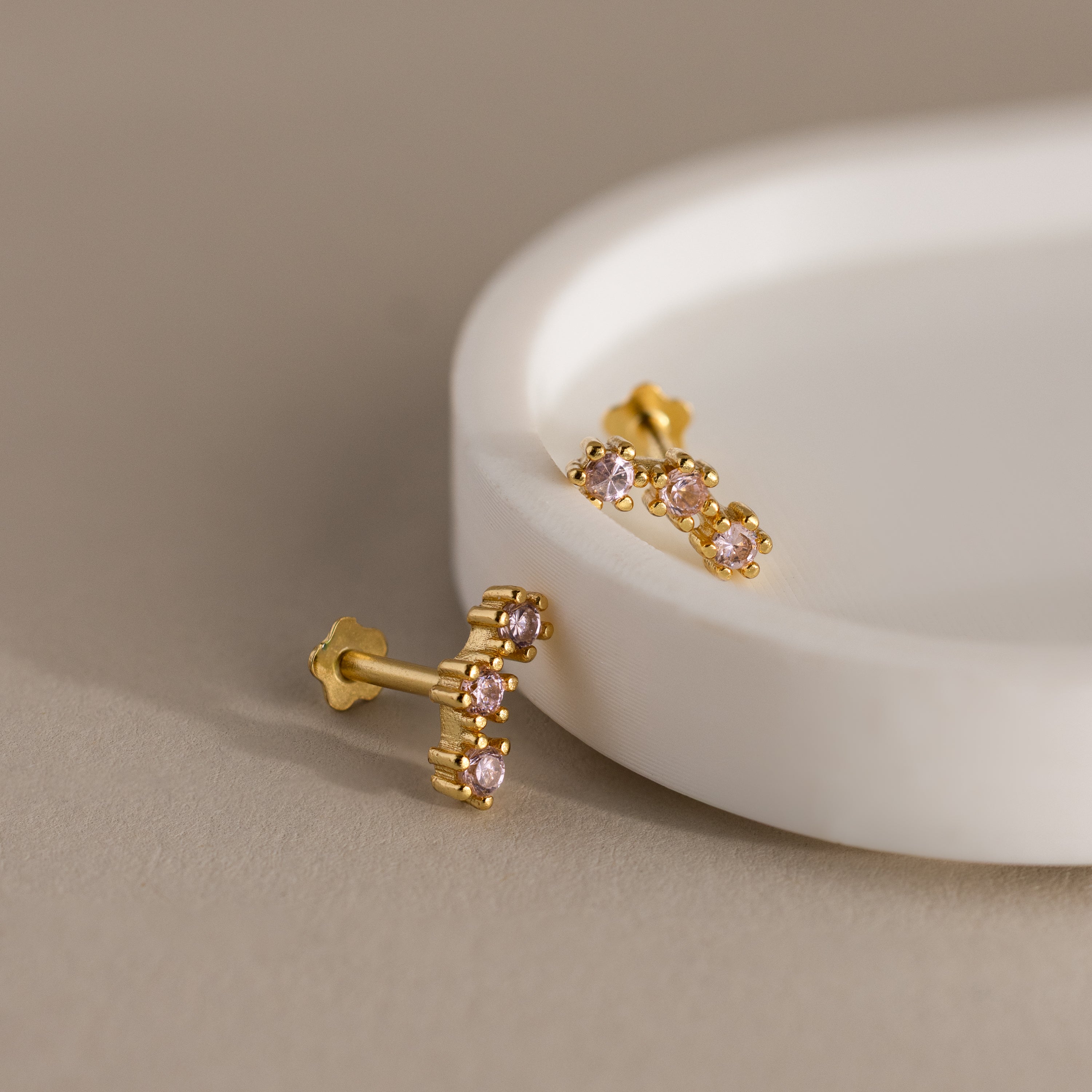 Sapphire Cluster Flatback Studs with pink gemstones are displayed on a round white dish against a beige background.