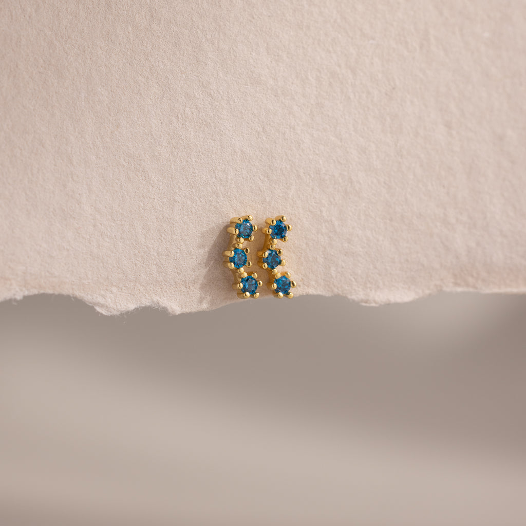 The Blue Zircon Cluster Flatback Studs are displayed on a textured, torn piece of off-white paper.