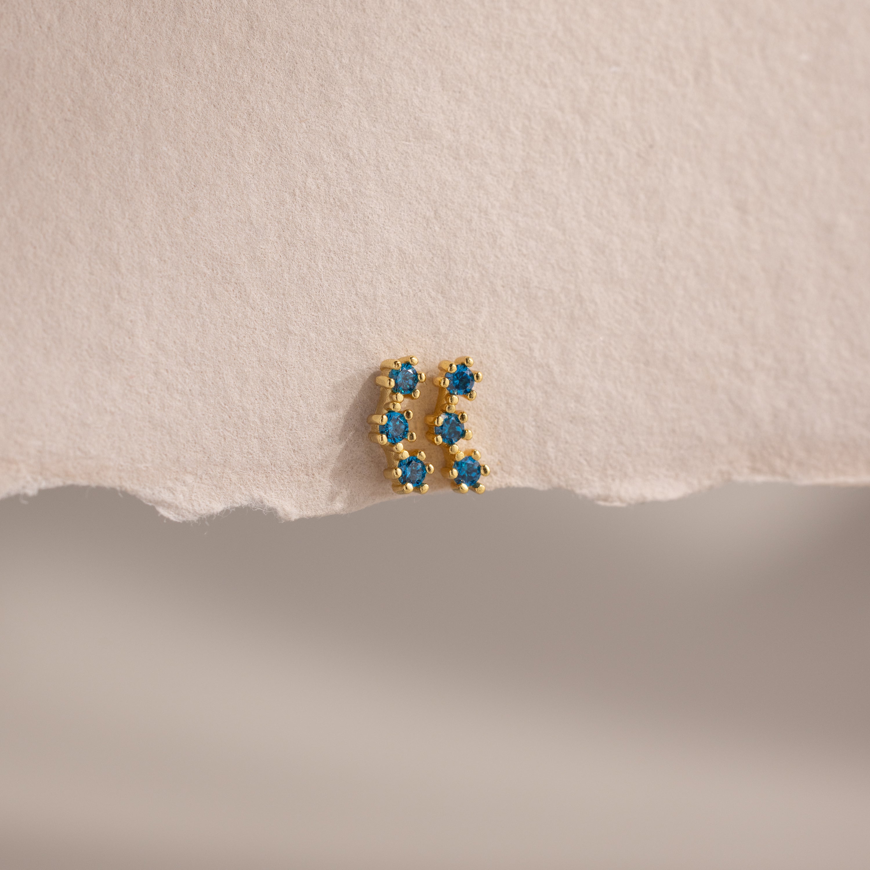 The Blue Zircon Cluster Flatback Studs are displayed on a textured, torn piece of off-white paper.