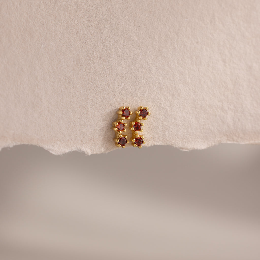 Garnet Cluster Flatback Studs, gold earrings adorned with red stones, styled on textured, torn beige paper.