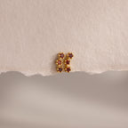 Garnet Cluster Flatback Studs, gold earrings adorned with red stones, styled on textured, torn beige paper.