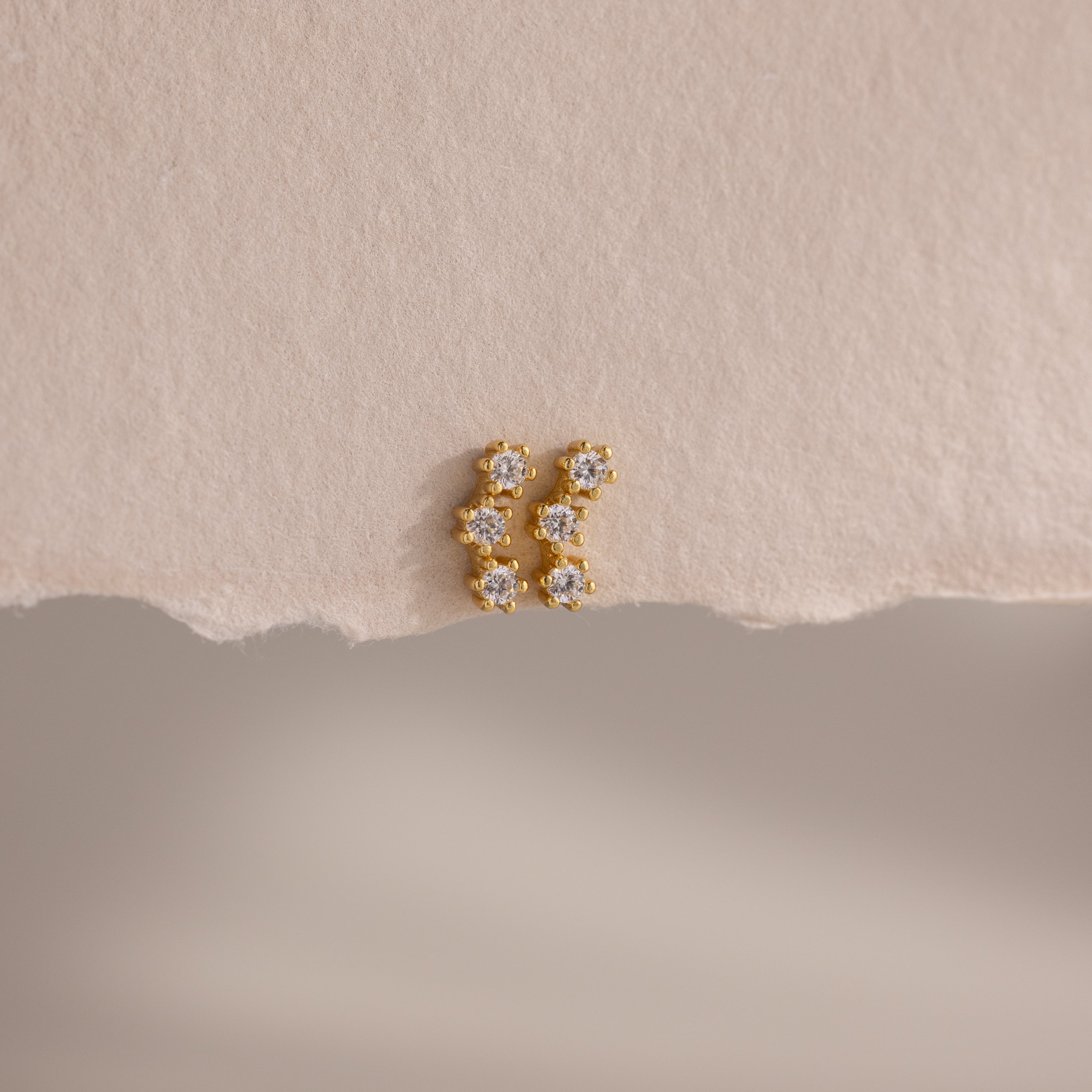 Diamond Cluster Flatback Studs with sparkling white gemstones are displayed on a textured beige surface.