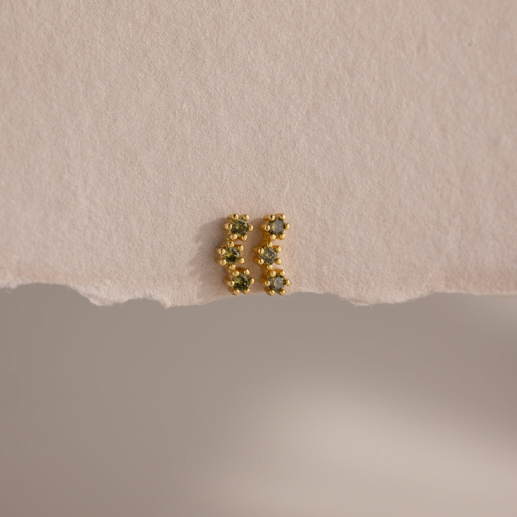 A pair of Peridot Cluster Flatback Studs with green gemstones rests elegantly on a textured, off-white surface.