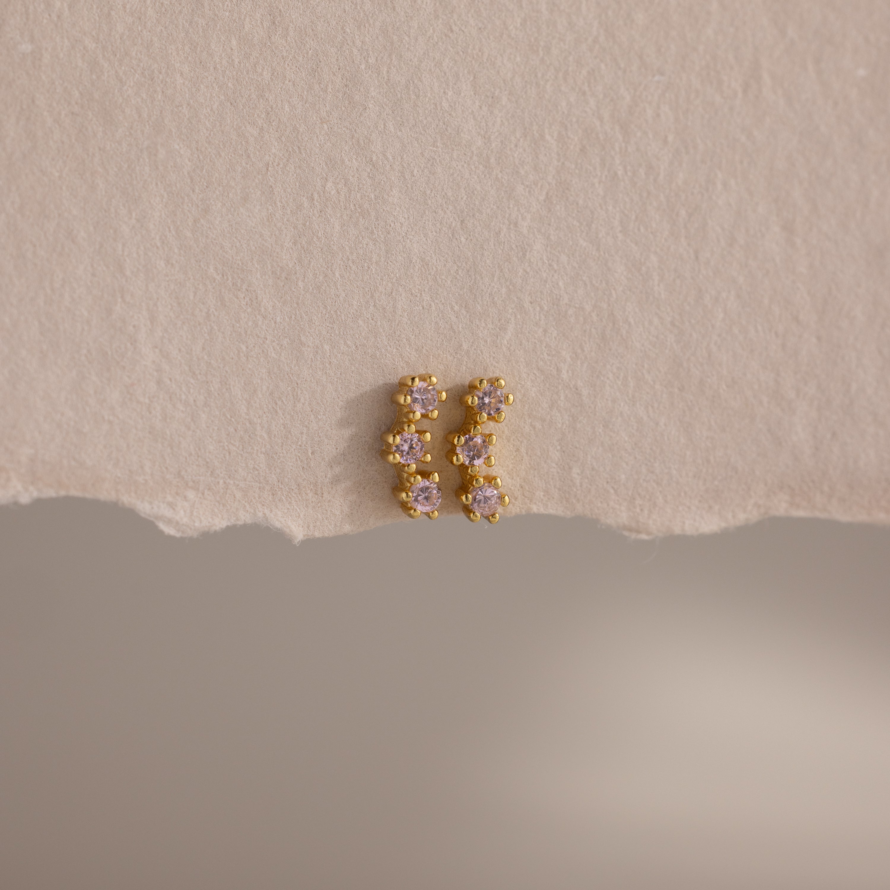 Pink Tourmaline Cluster Flatback Studs featuring small, pink stones are showcased on a textured, torn beige paper background.