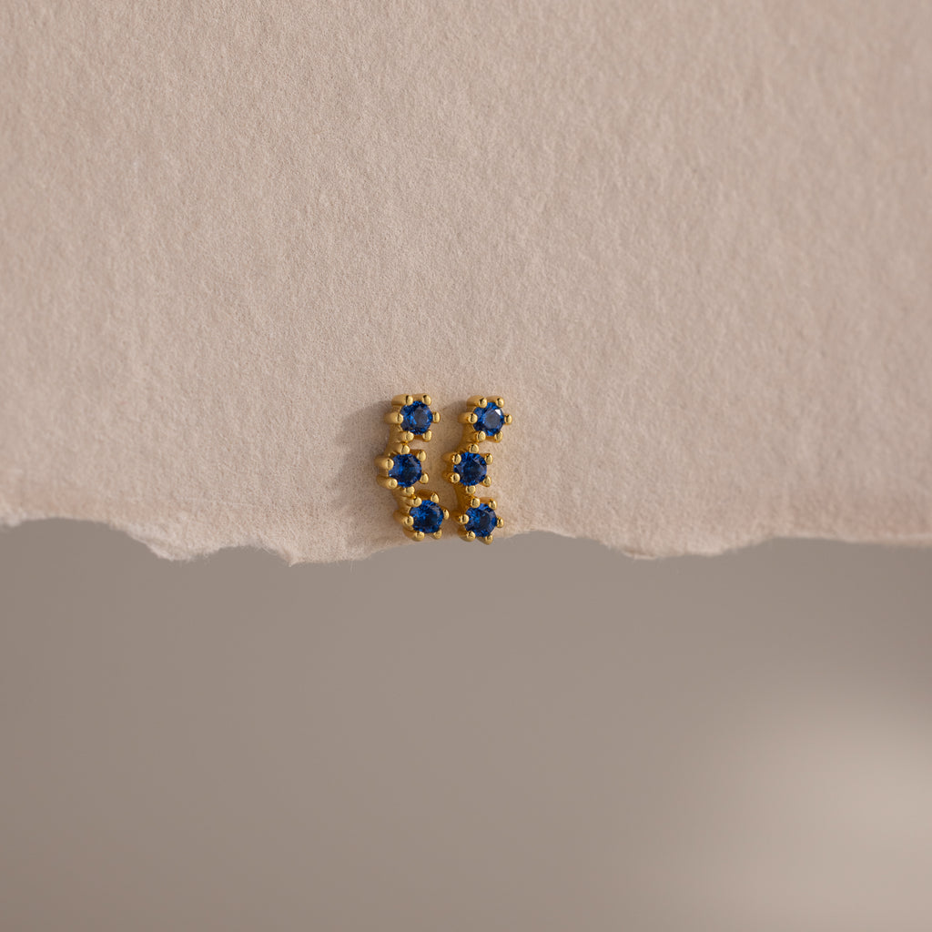 Sapphire Cluster Flatback Studs with small blue stones, photographed on textured beige paper with a torn edge—perfect for adding sparkle to your earring stack.