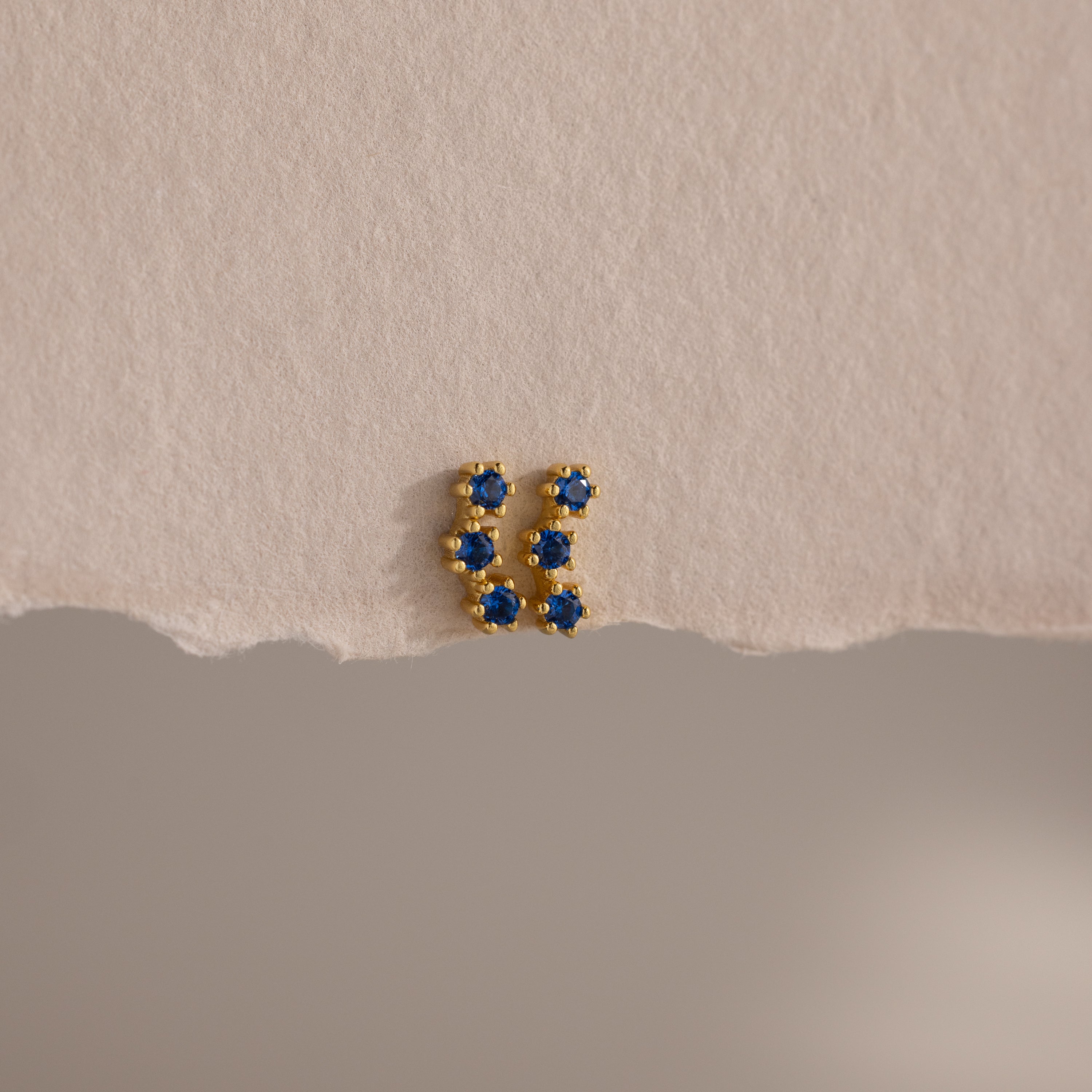 Sapphire Cluster Flatback Studs with small blue stones, photographed on textured beige paper with a torn edge—perfect for adding sparkle to your earring stack.