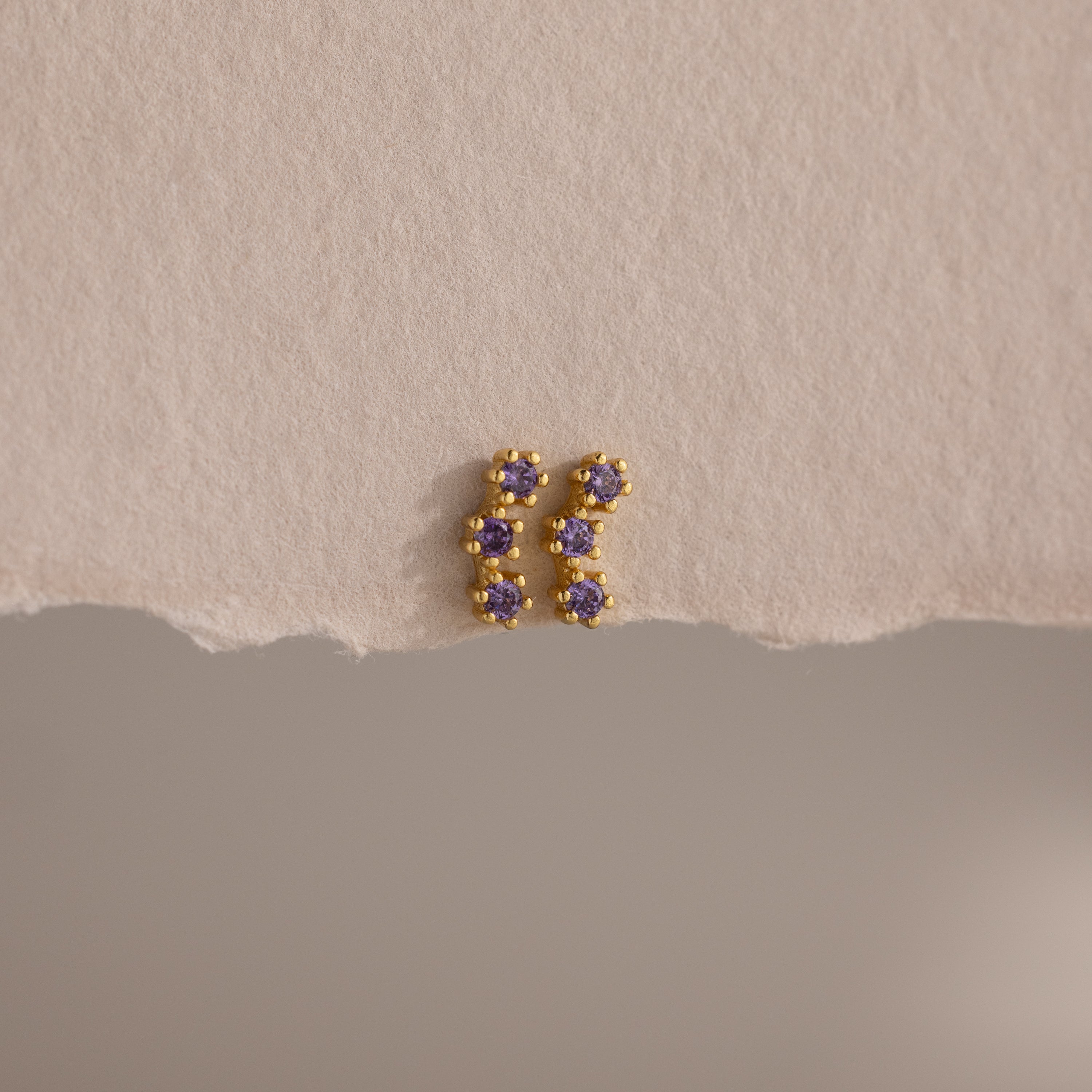 Amethyst Cluster Flatback Studs featuring small purple gemstones are displayed on a textured beige surface.