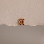 The Ruby Cluster Flatback Studs feature a small gold cluster design with six pink gemstones, shown on a textured beige surface.